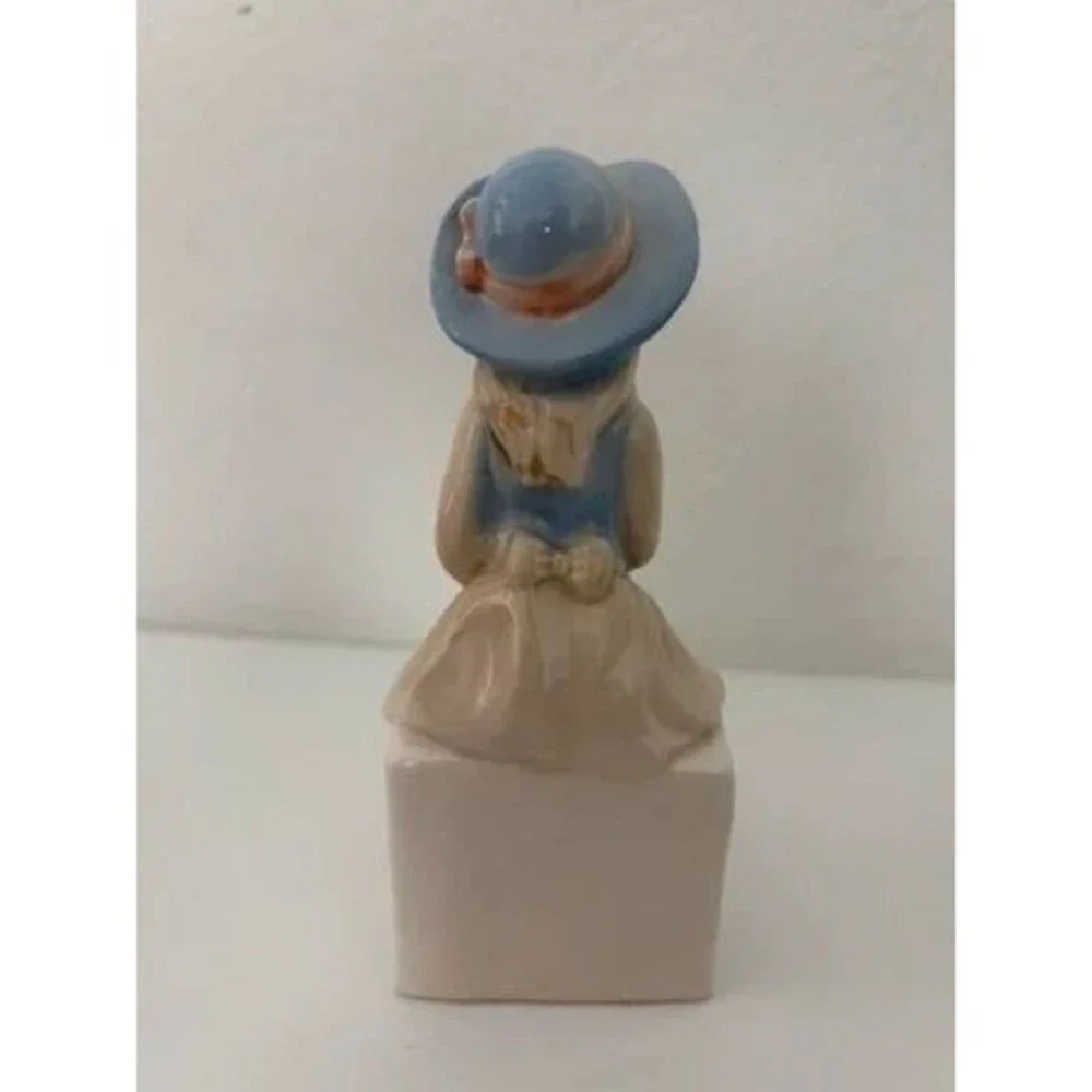 vtg. porcelain figurine of a seated girl wearing a blue hat